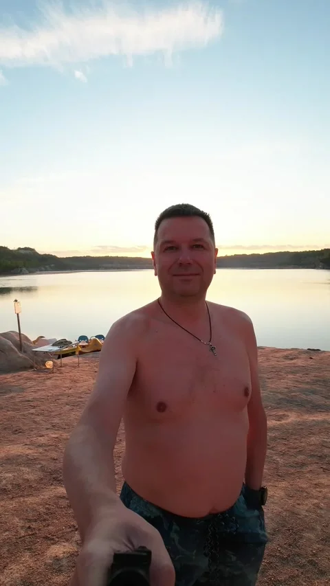 A man is taking a video selfie on a small, picturesque beach. Vertical Video Video stock 253892413