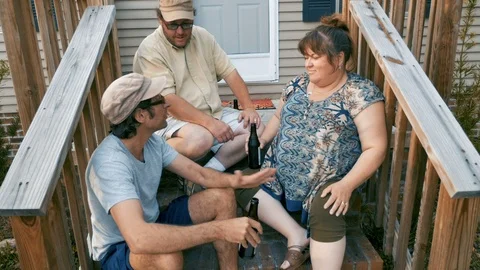 A man talking to another man and woman sitting on stairs in front of a house Stock Footage 87792873