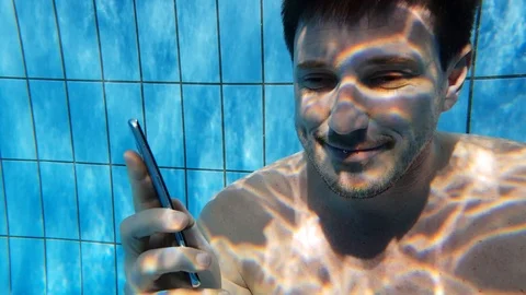 A man talking on a cell phone under water in a swimming pool Stock Footage 103324044