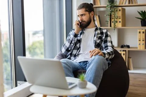 Man talking on cell phone while working from home with laptop Stock Photos
