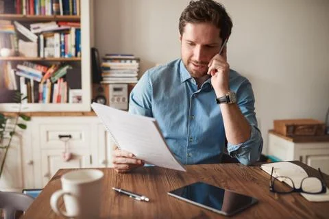 Man talking on a cellphone while reading paperwork at home Foto stock