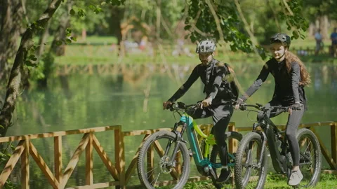 Man Talking to His Girlfriend as They Ride Bicycles by the Lake in the Park Stock Footage 252398650