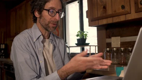Man talking to his laptop computer in his kitchen while video chatting Stock Footage 128177603