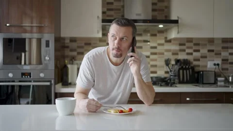A man talking on his mobile phone and smiling while eating pancakes in a mo.. Stock Footage 332287972