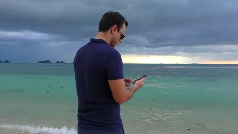 Man talking on his smart phone on the beach in cloudy dark weather Stock Footage 81493956