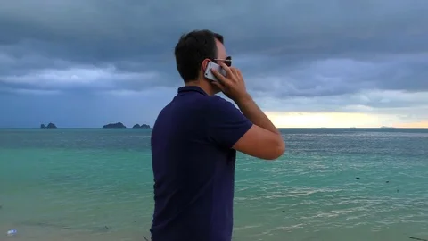 Man talking on his smart phone on the beach in cloudy dark weather Stock Footage 81496064