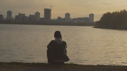 A man talking on a mobile phone and sits on the shore of the lake. Stock Footage 99388913