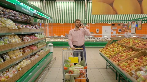 Man talking to mobile phone while standing with trolley in food store Stock Footage 63431343