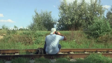 A man talking on a mobile phone while sitting on the Soviet old railway rail 库存影片 205250302