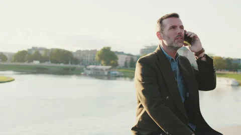 Man talking on mobile phone while sitting on the embankment on the river Stock Footage 227134123