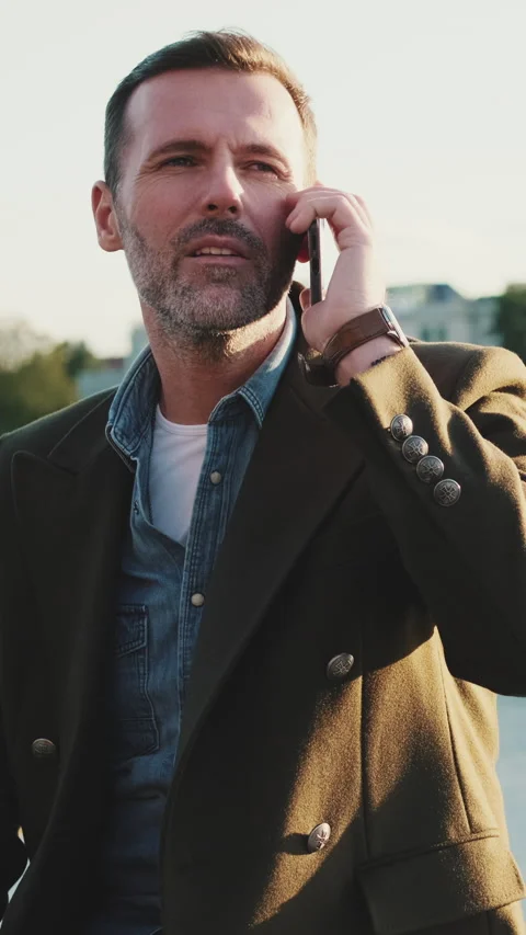Man talking on mobile phone while sitting on the embankment on the river. Stockbeeldmateriaal 227135565