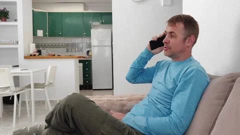 A man talking on a mobile phone while sitting on the sofa in a large bright Stock Footage 276921196