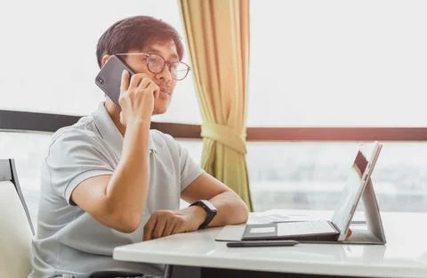 Man talking on mobile phone while working laptop computer. Stock Photos