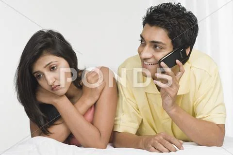 Man talking on a mobile phone with a woman looking sad beside him Stock Photos