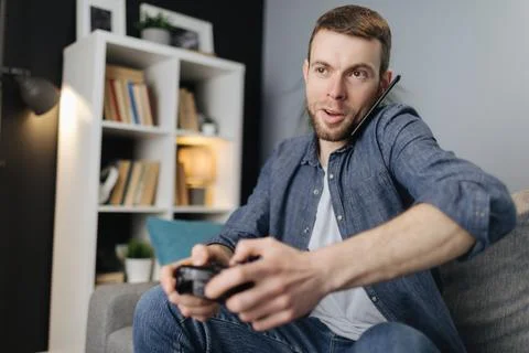 Man talking on mobile while playing video games Stock-Fotos