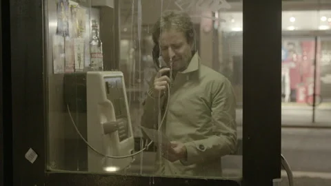 Man Talking on a Payphone Inside a Booth at Night Stock Footage 344620062
