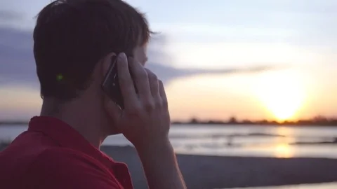 Man talking on the phone, against the background of the river at sunset. HD Stock Footage 80859266