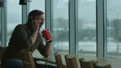 Man talking on the phone and drinking in a cafe near the window. Video stock 73341505