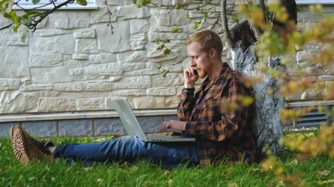 Man talking on the phone and working on a laptop while sitting in the garden Stock Footage 200825338
