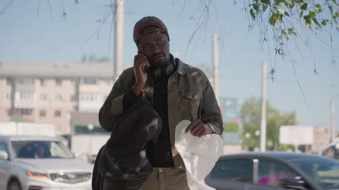 Man talking on phone holding paper and bag outdoors with cars passing by in Stock Footage 345839690