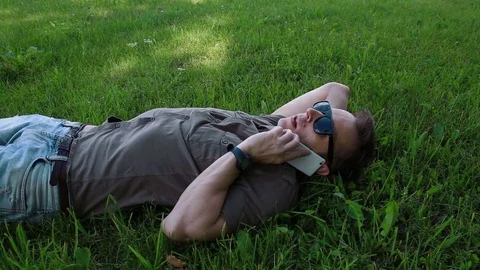 Man talking on the phone lying on the grass 스톡 동영상 76741189