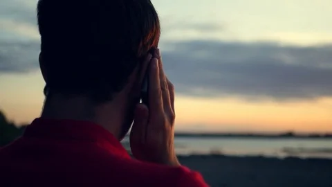 A man is talking on the phone, by the river at sunset. HD, 1920x1080. slow Stock Footage 80859246