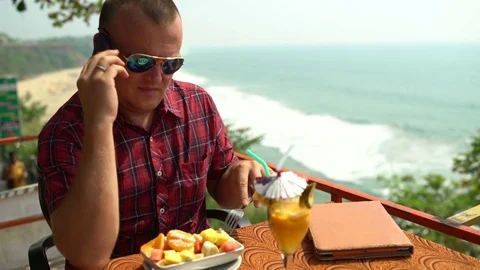 Man talking on the phone sitting in a cafe and eating fruit salad Video stock 74759836