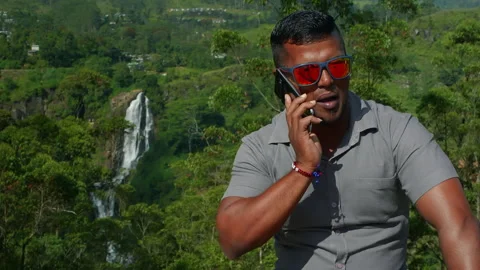 Man talking on phone with waterfall in background Stock Footage 318640386