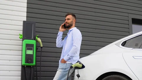 A man talking on the phone while charging luxury electric car at charging Stock Footage 251765567
