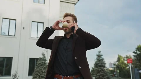 Man talking on the phone while enjoying a coffee outside a modern building 스톡 동영상 303798376