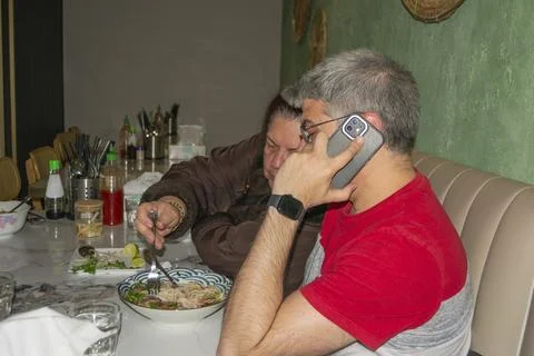 Man talking on phone while having lunch with woman in Vietnamese restaurant Stock Photos