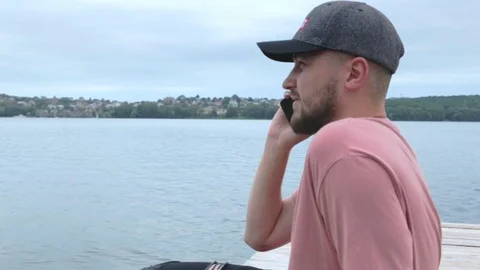 Man talking phone while sitting near wide lake in slow motion Stock Footage 91726299