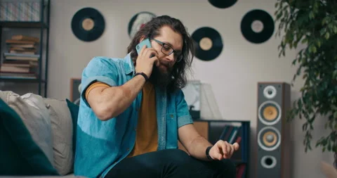 A man is talking on the phone while sitting on the couch with his dog. He 動画素材 218192943