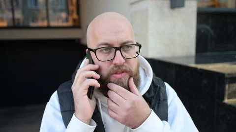 Man talking on phone while sitting outside in urban setting, showing deep Stock Footage 346551200