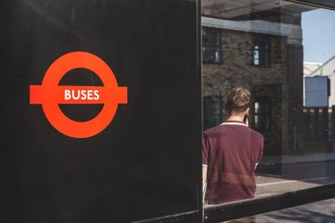 A man talking on a phone while waiting for a bus at a bus stop in London Stock-Fotos