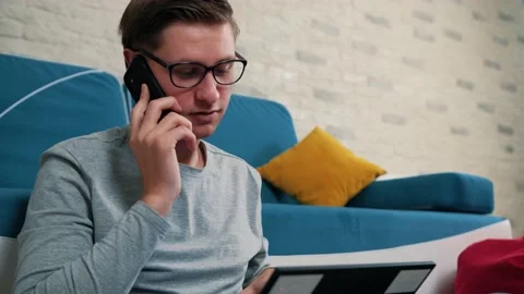Man talking on phone while is working on laptop, sitting on bean bag at home. Stock Footage 146238057
