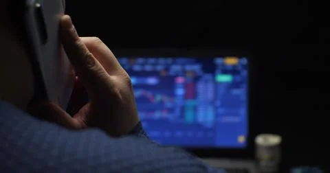 A man is talking on the phone while working on a laptop with bitcoins. Buying Stock Photos