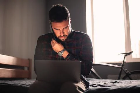 Man talking on smart phone using laptop computer working at home Foto stock