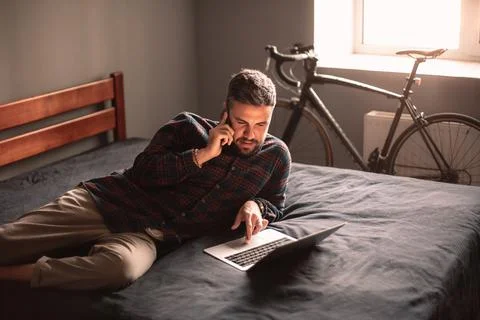 Man talking on smart phone while using laptop computer working at home Foto stock