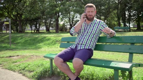 Man talking by smartphone, on bench in park. Steadicam. Vidéo 67235143