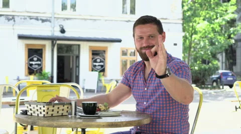Man talking by smartphone during breakfast, shows ok to camea 库存影片 67627343