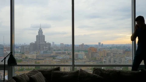 Man talking on the smartphone enters frame and exits near the panoramic window Stock Footage 103200140