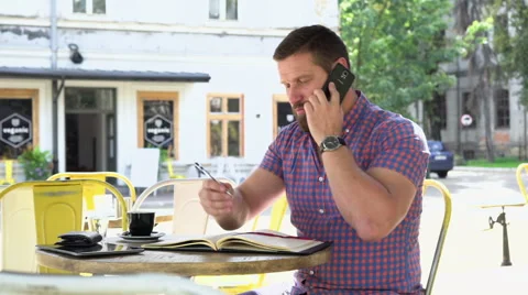 Man talking by smartphone makes notes to notebook, slider shot, left 動画素材 67629769