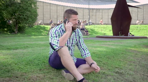 Man talking by smartphone, sitting on grass. Steadicam. Vídeo Stock 67236218