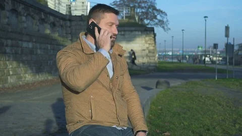 Man talking by smartphone sitting on wall at boulevard next to river  Vídeo Stock 72775233