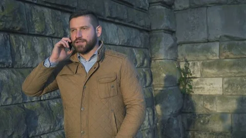 Man talking by smartphone, walking along the old wall, steadicam, outdoor Vídeo Stock 72775551