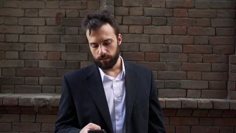 Man talking by smartphone, walking along the old wall, steadicam, outdoor Видео 77015716