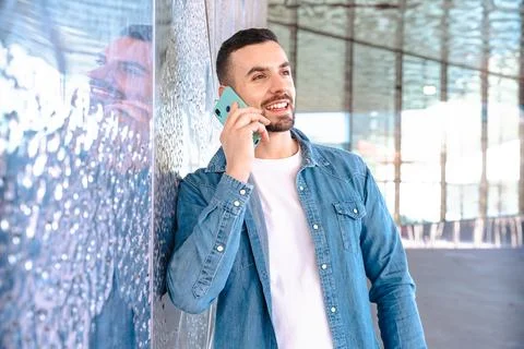 Man talking on smartphone while leaning against glass wall in modern building Stock Photos