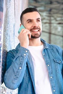 Man talking on smartphone while leaning against glass wall in modern building Stock-Fotos