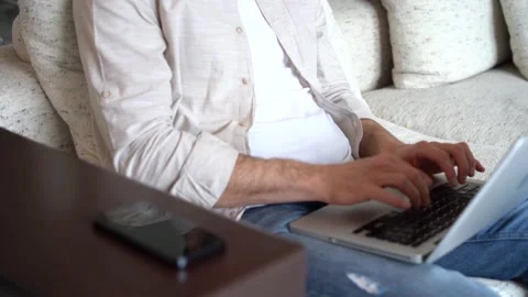 Man talking on smartphone while sitting on couch with laptop, working remotely Video stock 154796372